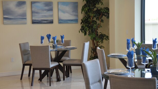 A dining area with tables set for four, chairs, and a large potted plant. - The Sands (Sauble Beach)
