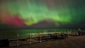 A nighttime view of the Northern Lights over a waterfront area with benches and a fence. - The Sands (Sauble Beach)