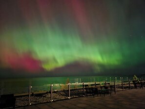 A nighttime view of the Northern Lights over a waterfront area with benches and a fence. - The Sands (Sauble Beach)