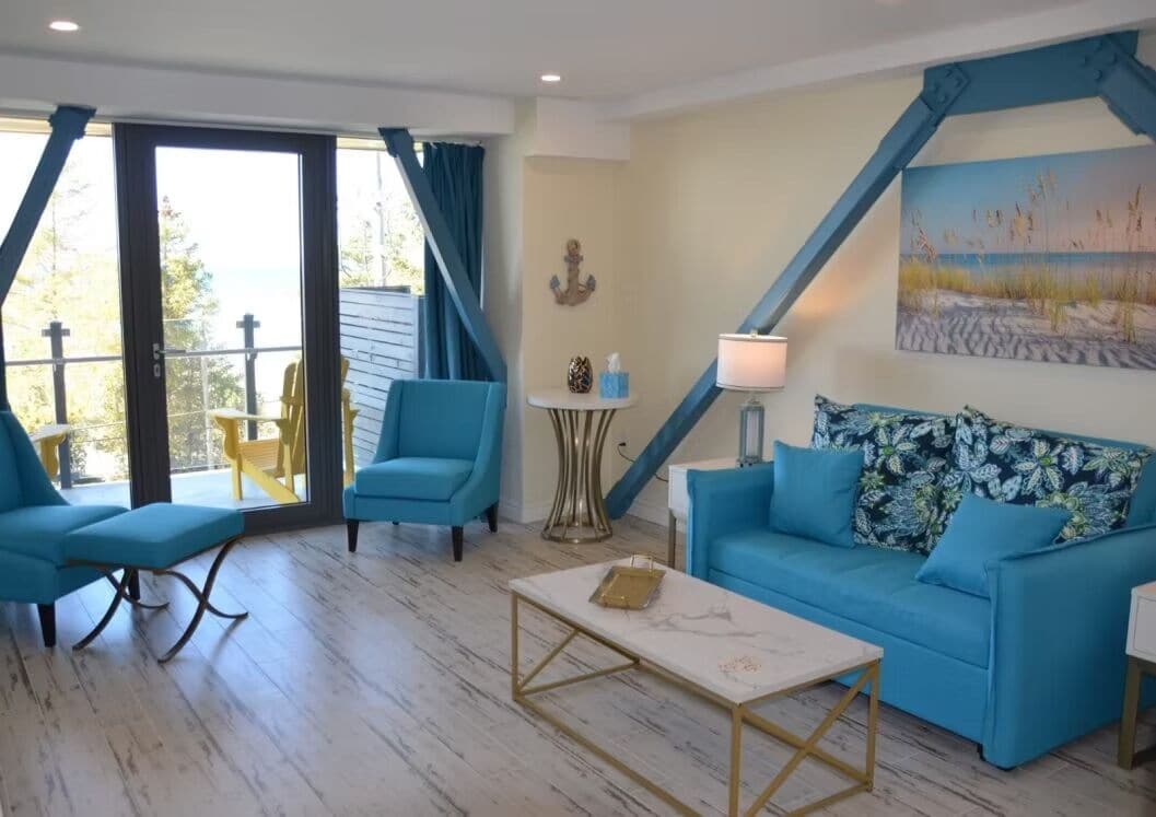 A living room with a blue sofa, matching armchairs, a coffee table, and a painting of a beach scene.