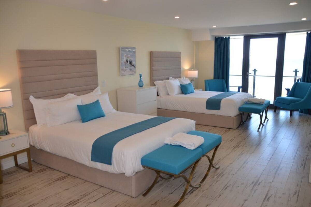 A hotel room with two beds, a seating area, and a balcony with a view.