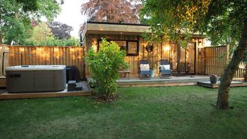 A wooden cabin with a hot tub, two lounge chairs, and a small deck.