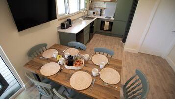 A dining area with a wooden table set for six, surrounded by six chairs. A flat-screen TV is mounted on the wall above the table.