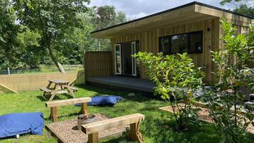 A modern wooden cabin with a deck, picnic tables, and a small garden area.