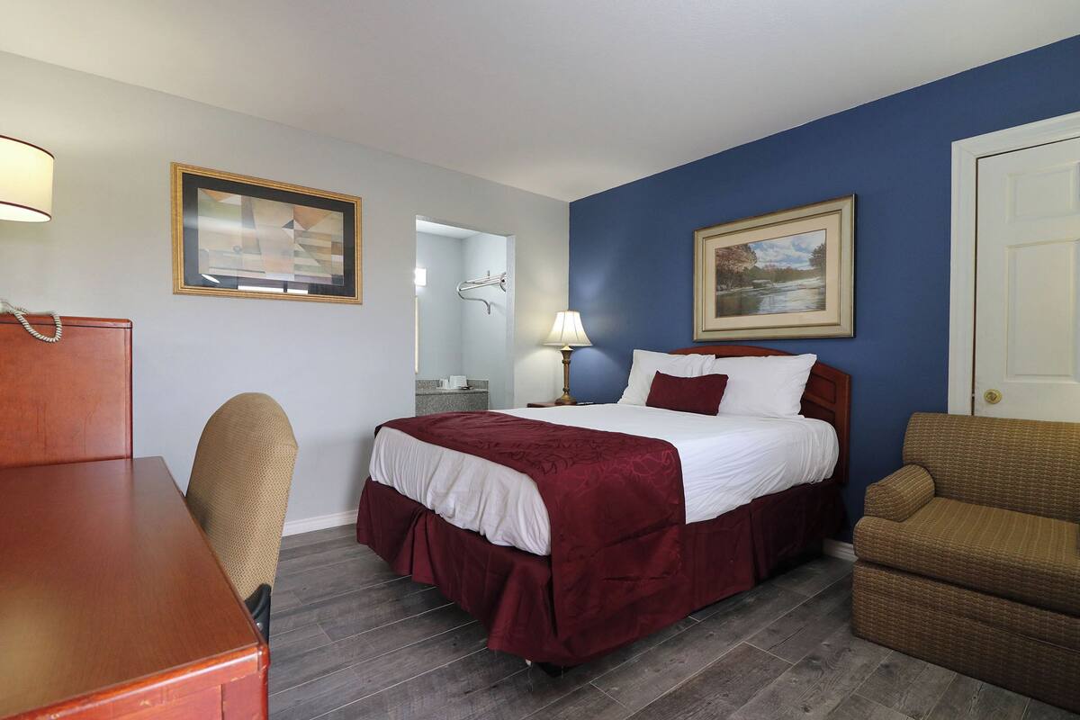 A hotel room with a bed, a desk, a chair, a nightstand, and a lamp.