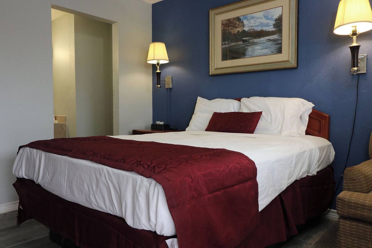 A hotel room with a large bed, two bedside lamps, a framed picture on the wall, and a chair.