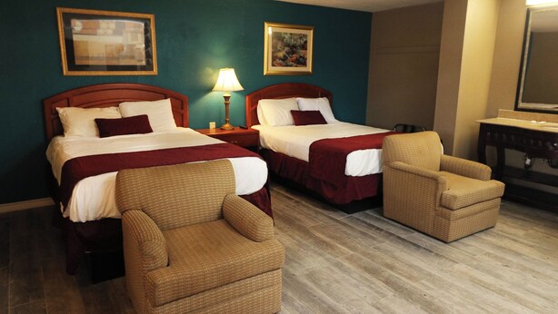 Ein Hotelzimmer mit zwei Betten, einem Sofa, einem Sessel, einem Schreibtisch und einem Spiegel.