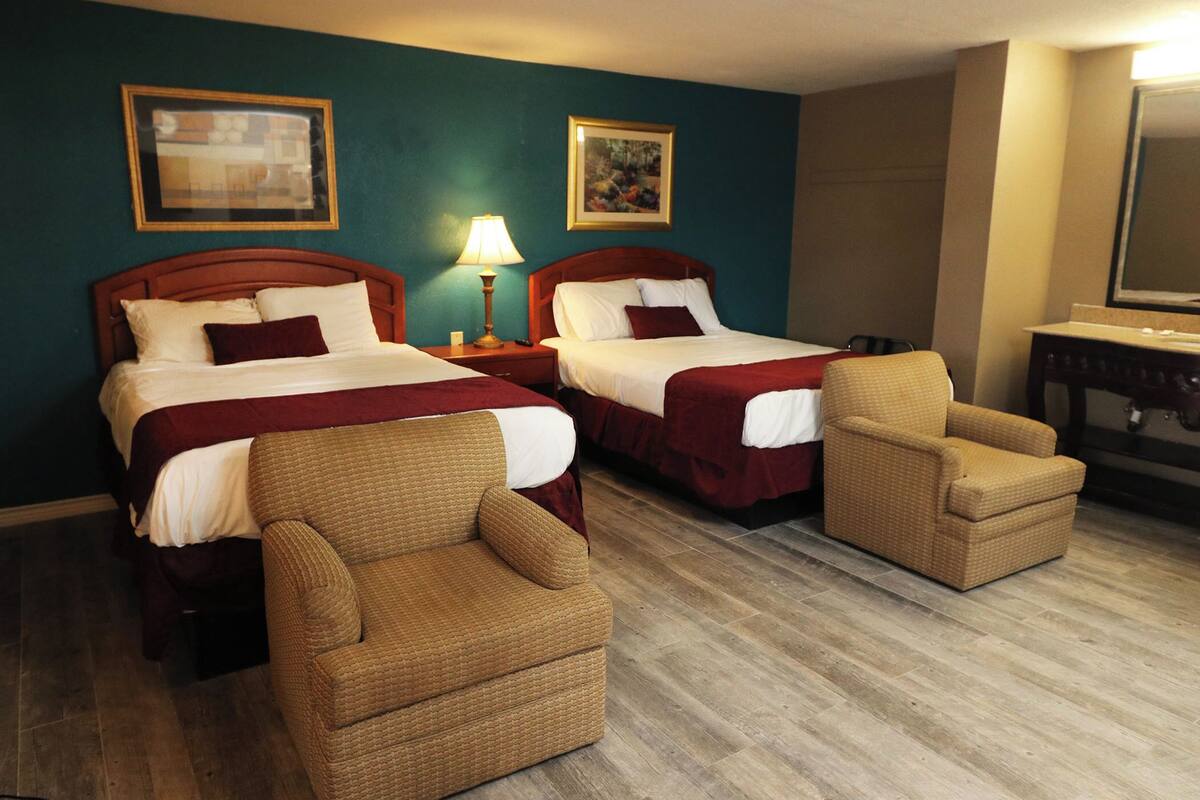 A hotel room with two beds, a sofa, a chair, a desk, and a mirror.