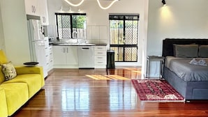 A modern living space with a kitchen, a yellow sofa, a grey sofa, and a red rug. - Garden Retreat with Pool - fully detached Studio (Freshwater)