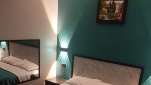 Habitación de hotel con paredes color turquesa, una cama con ropa blanca, un cuadro en la pared y una toalla doblada sobre la cama.