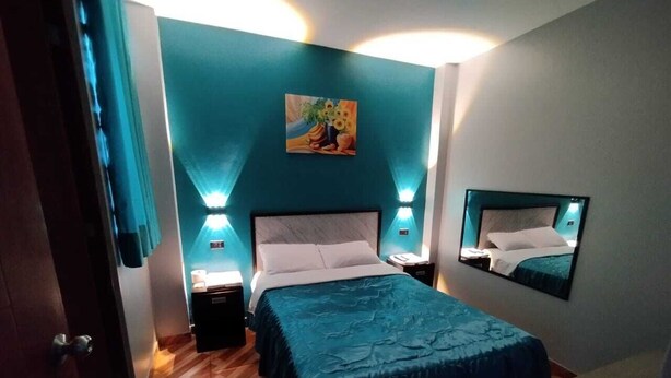Un dormitorio con cama, mesitas de noche, un cuadro y un espejo.
