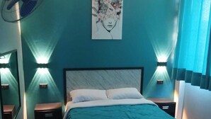 Un dormitorio con cama, mesitas de noche, un ventilador de pared y un cuadro.