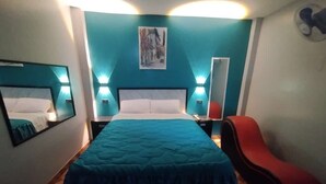 Un dormitorio con una cama grande, dos mesitas de noche, una silla roja y un espejo fijado a la pared.