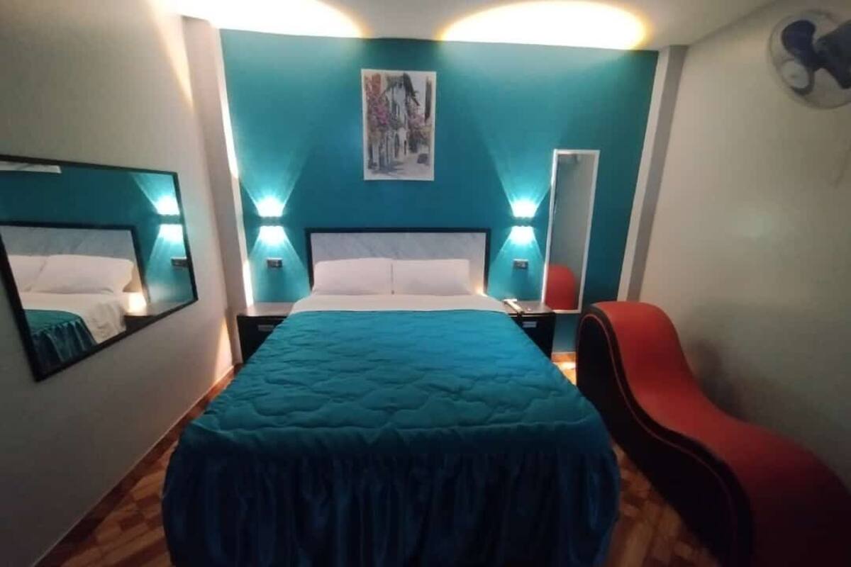 A bedroom with a large bed, two bedside tables, a red chair, and a wall-mounted mirror.