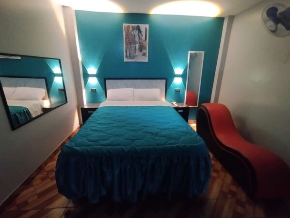 A bedroom with a large bed, two bedside tables, a red chair, and a wall-mounted mirror. - Hostal El Pilar (Callao)