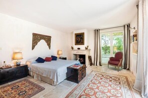 Relax in this inviting bedroom with a large bed, nightstands, and a fireplace, offering a comfortable seating area and a view of the outdoors.