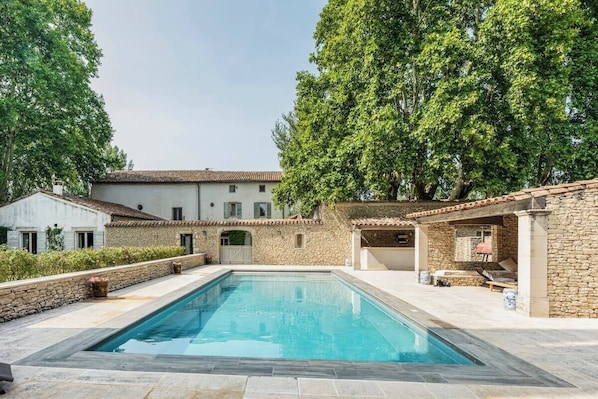 Relax by the serene pool surrounded by lush greenery and a traditional building in the background.