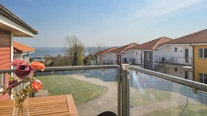 A balcony with a view of the sea, a wooden table, and a vase of flowers. - Gudhjem Søpark Lejl. 42 (Gudhjem)