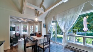 A dining area with a wooden table and chairs, a basket, and a view of a garden through large windows. - Chalet SUR LE Lac, A Quelques PAS DU LAC St-louis (Dorval)