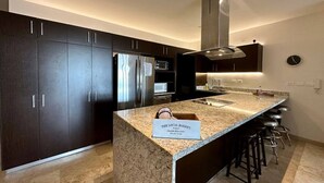 Una cucina moderna con mobili scuri, elettrodomestici in acciaio inossidabile, un piano di lavoro in granito e un cartello che indica una panetteria.
