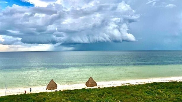 Una spiaggia con ombrelloni di paglia e vista sull'oceano sotto un cielo nuvoloso.