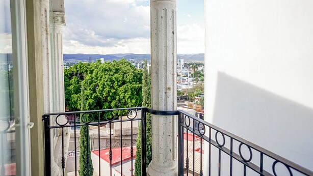 A balcony with a view of a cityscape, including buildings and a tree.