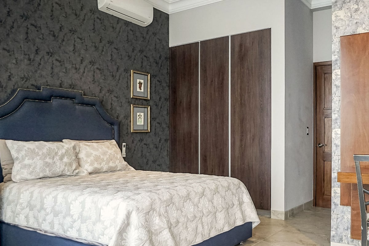 Ein Schlafzimmer mit einem Bett, einem Kleiderschrank, einem Sessel mit Ananas-Dekoration und einem Regal mit einer Büste.