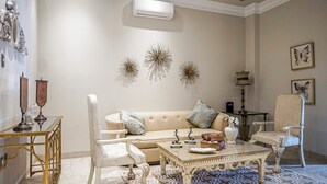 A living room with a beige sofa, white armchairs, a patterned rug, and decorative wall art.