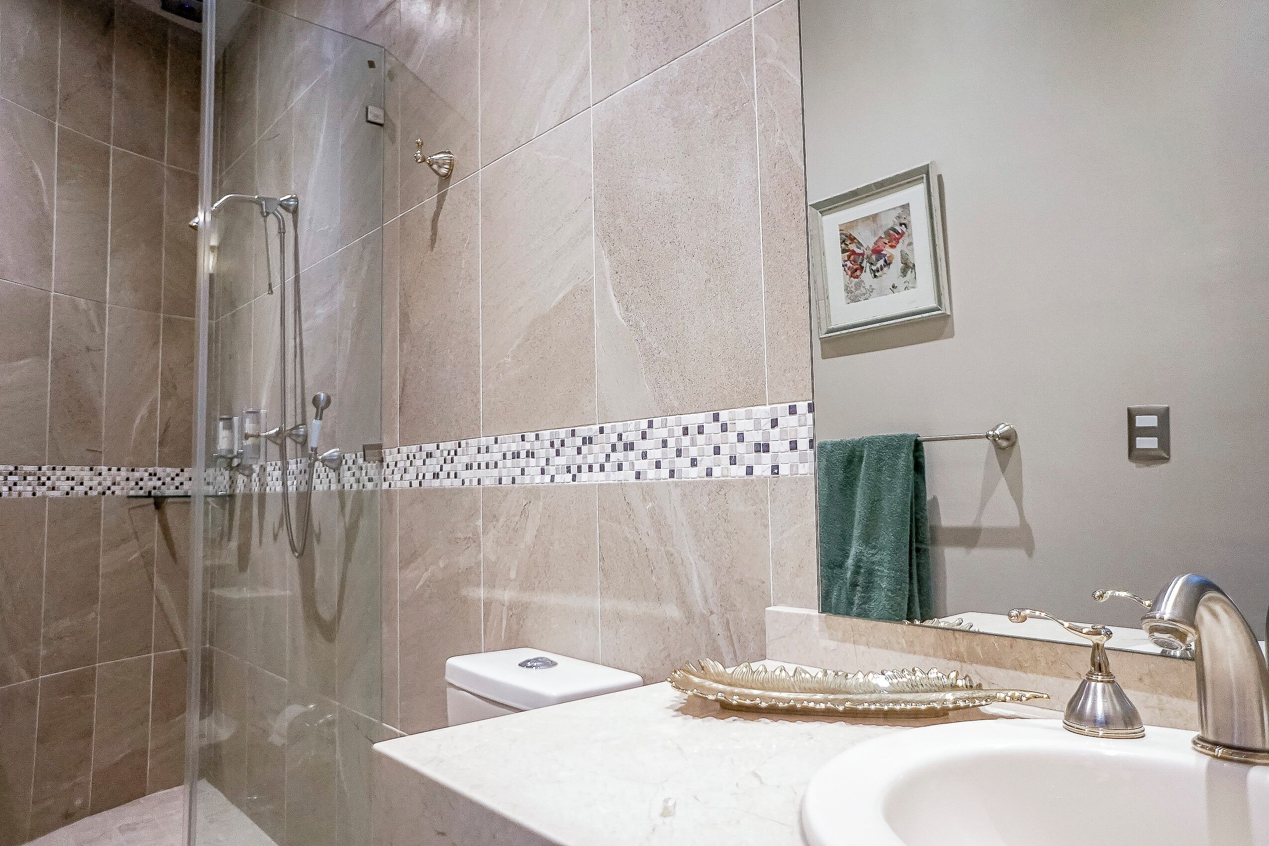 A modern bathroom with a glass-enclosed shower, a white sink with a decorative tray, and a tiled backsplash.