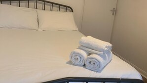 A neatly made bed with white linens and rolled towels, a black metal headboard, and a closed door in the background. - Cosy 2 Bedroom Gem near Oxford Street (London)