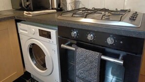 A compact kitchen with a washing machine, a microwave, a toaster, and a gas stove. - Cosy 2 Bedroom Gem near Oxford Street (London)