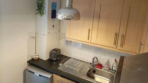 A kitchen with wooden cabinets, a stainless steel sink, a toaster, a kettle, and a dish rack. - Cosy 2 Bedroom Gem near Oxford Street (London)
