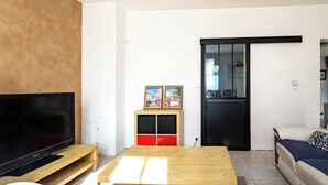 A modern living room with a flat-screen TV, wooden coffee table, and a sofa. There is a cabinet with red and black panels and a door with a glass panel. - Parenthèse Tourangelle - Families & Business (Tours)