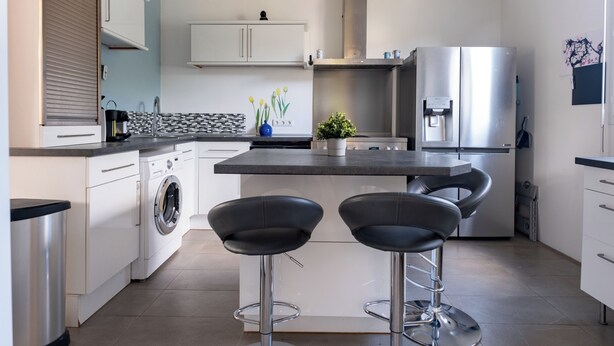 A modern kitchen with a built-in washing machine, a stainless steel refrigerator, and two bar stools. - Parenthèse Tourangelle - Families & Business (Tours)