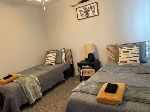 A bedroom with two single beds, each with a bedside table, a lamp, and a wall-mounted sign.