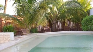 A rectangular pool with clear water, surrounded by a wooden fence and palm trees. - Casa Del Mar.  (Chelem)