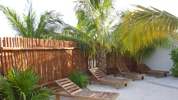 A sandy outdoor area with wooden lounge chairs and a bamboo fence. - Casa Del Mar.  (Chelem)