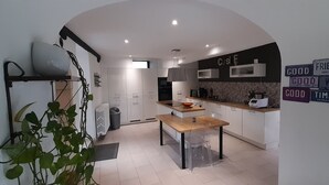 A modern kitchen with white cabinets, a wooden countertop, and a dining area with a table and chairs. There are potted plants and a wall with motivational signs.