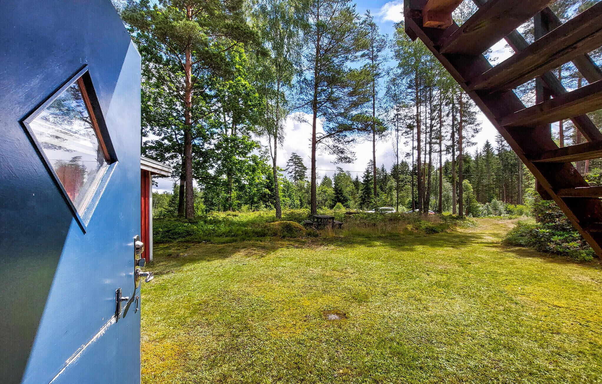 A blue door with a window, a wooden deck, and a grassy yard with trees in the background.