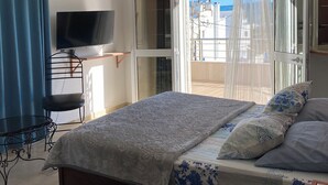 Une chambre à coucher avec un lit, une télévision, un bureau et un balcon avec des rideaux.