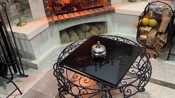 Une cheminée avec un feu crépitant, une table ronde à structure métallique et des objets décoratifs sur le manteau de la cheminée.