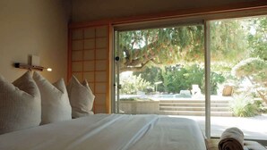 Una camera da letto con un letto grande, vista su un giardino e una porta scorrevole in vetro.