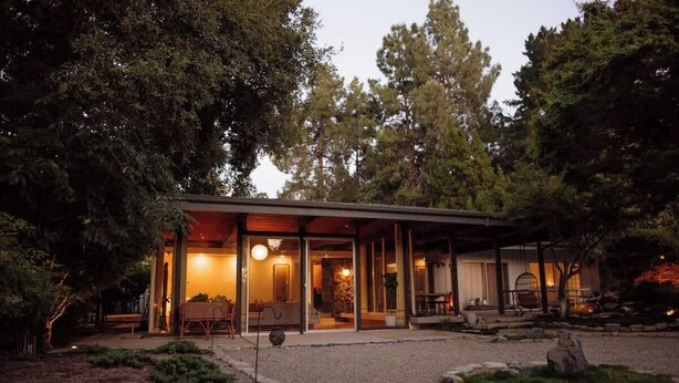 Una casa moderna con patio coperto, circondata da alberi e vialetto in ghiaia.