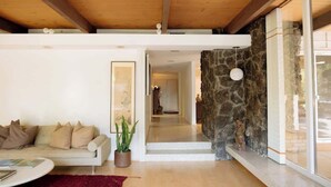 Un soggiorno moderno con soffitto in legno, una parete decorata in pietra, un divano con cuscini, una pianta in vaso e un tappeto rosso.