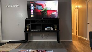 A living room with a flat-screen TV on a black stand, a coffee table with magazines, and a hallway to the right. - ~A Home Away From Home~Sleeps 8~

 (Columbia)