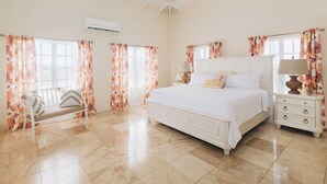 Un dormitorio con una cama grande, una mesita de noche con lámpara, una silla y cortinas con motivos florales.