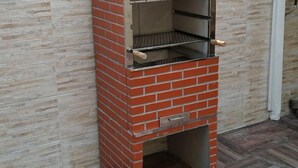 A brick-built outdoor oven with a chimney, a metal shelf, and a handle, set against a tiled wall and wooden flooring. - Copacabana Comfort Home (Rio de Janeiro)