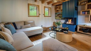 Una sala de estar acogedora con un sofá, una mesa redonda, una chimenea y estanterías de madera llenas de libros.