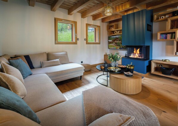 A cozy living room with a sofa, a round coffee table, a fireplace, and wooden shelves with books.
