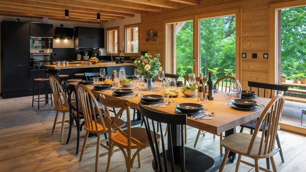 Una cocina moderna con una isla central, ventanas amplias y un comedor preparado para seis personas.